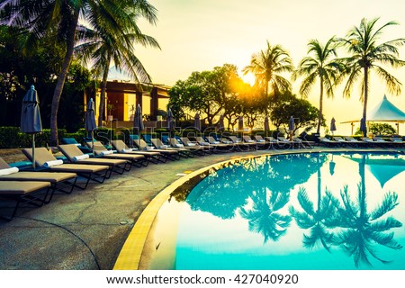 Beautiful luxury umbrella and chair and coconut palm tree around outdoor swimming pool in hotel resort at sunrise time - Vintage filter and boost up color Processing