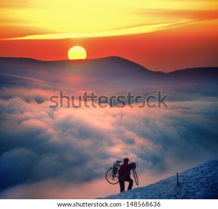 Cyclist extreme, during a beautiful sunrise raises road bike to the top of the mountain where there is snow