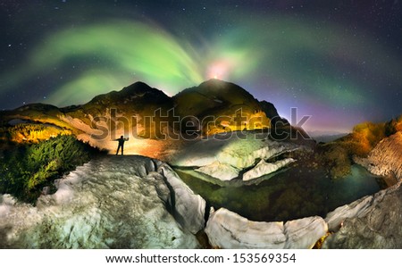 Flashes of the Northern Lights. Moon over the top of Pop Ivan Maramorosh and lonely figure, drawing a powerful LED flashlight pictorial compositions of the alpine lake, where icebergs float
