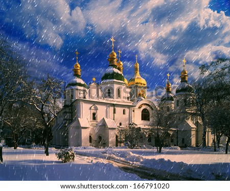 White flakes falling on the old Ukrainian monastery fell asleep paths and trails on the background, and only a sunbeam falls from the sky on the dome of an Orthodox church
