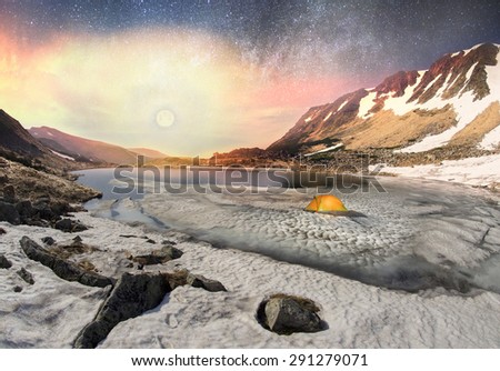 In the spring a group of tourists spend the night in the snow and ice alpine lake Berbeneskul Montenegrin ridge of the Carpathians, in the starry sky galaxy at moonrise