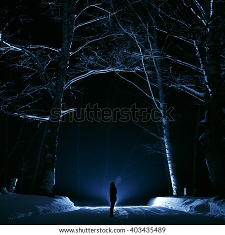 A girl or a guy in the woods one night. Forest winter dark and gloomy. The picture was taken with backlighting and blue. for banner Halloween or esoteric, gothic. Romania