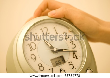 An alarm clock with a woman\'s hand to stop the noise