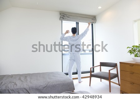 Young man in pajama standing beside the window and stretching