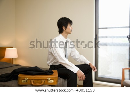 A young businessman sitting on the bed and looking at window