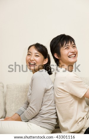A young couple sitting on the sofa back-to-back and smiling