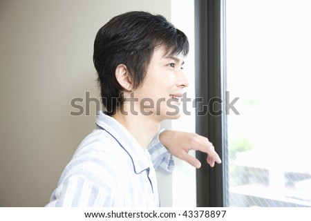 Young man in pajama standing beside the window and looking at outside