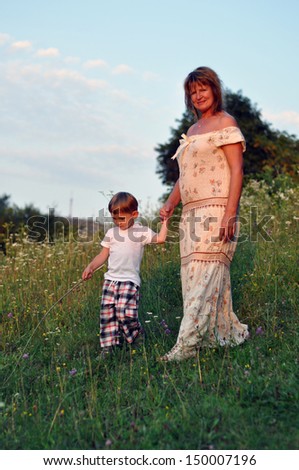 Grandmother and grandson walk on the field during summer