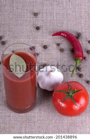 Glass of tomato juice with tomato, garlic, bay leaf and pepper on the sackcloth background