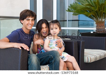 Three beautiful children sit happily together on a patio chair at a luxury hotel, enjoying each other\'s company.