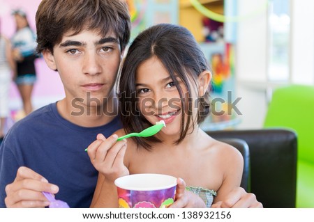 Beautiful brother and sister sit down together and share a delicious frozen yogurt at a restaurant