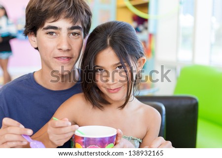 Beautiful brother and sister sit down together and share a delicious frozen yogurt at a restaurant