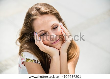 Outdoor portrait of young happy woman dreaming - hands under chin