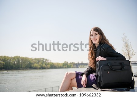 Young smiling business woman portrait with notebook bag - sitting in nature