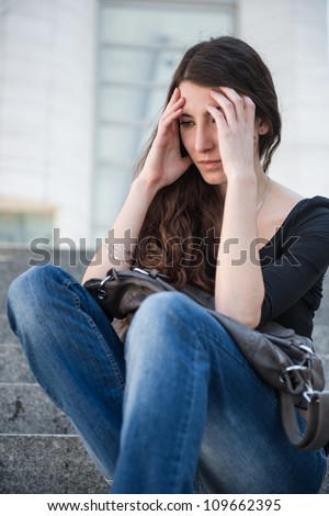 Young woman with headache - sitting outdoor holding head