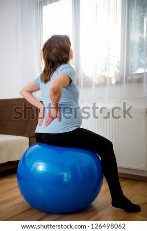 Pregnant woman sitting on fit ball with backache at home