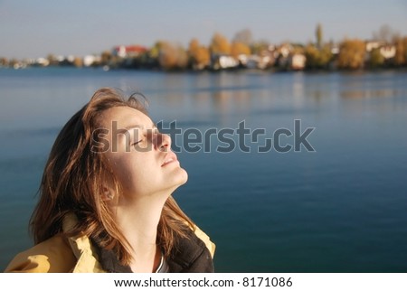 Pretty young woman with face turned to sun with beautiful water autumn (fall) background