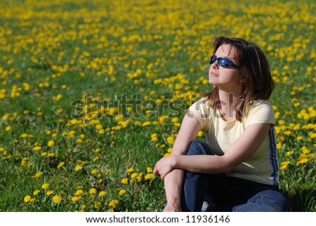 Woman in sunglasses sitting in field of dandelions with face turned to sun