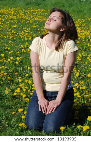 Woman on knees in field of dandelions with face turned to sun