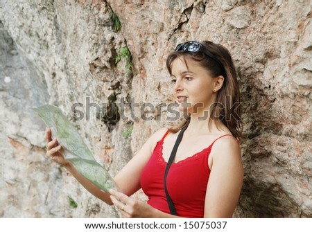 Young woman at rocky wall looks to map and wants to find way