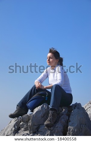 Young woman on top of mountain relaxes on rocks with blue sky