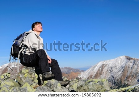 Hiker relaxing on rocky hill with clear blue sky with face turned to sun