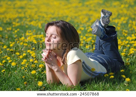 Woman lying in field of dandelions with face turned to sun