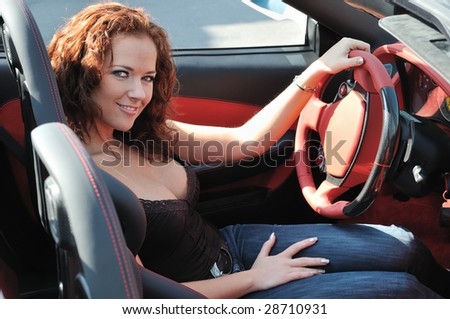 Young beautiful happy woman in sport car holding steering wheel - red interior detail