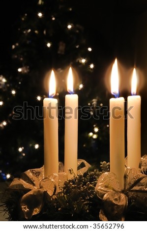Christmas advent wreath with burning candles. Lights on x-mas tree in background