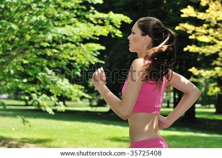 Young beautiful woman in pink running (jogging) outside in park on sunny day