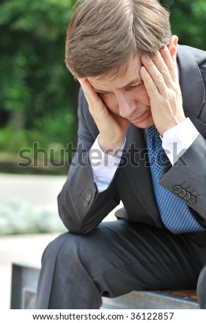 Portrait of depressed senior business man with head in hands siting on bench outdoors