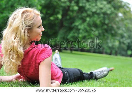Young smiling woman relaxing in green grass after roller skating - rear view