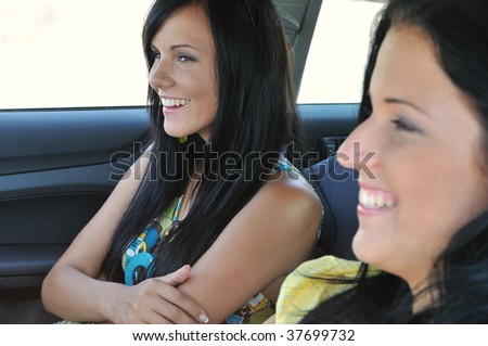 Youth lifestyle - two laughing friends (teenagers) driving in car, focus on farther girl
