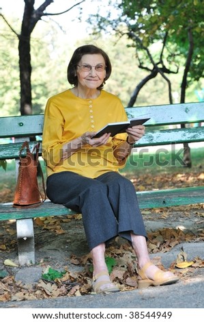 Senior woman sitting on bench reading book outdoors in park
