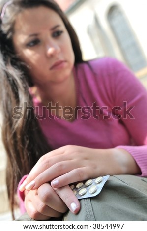Take or not - young woman  (teenage girl) decides while holding pills, focus on hands