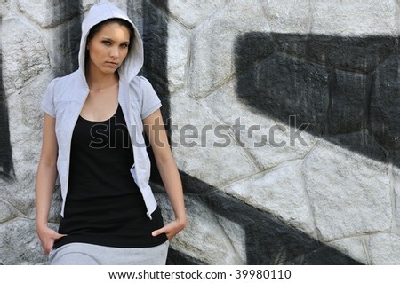 Young person (teenage girl) with hood in hip hop style standing at black and white graffiti wall with copy space