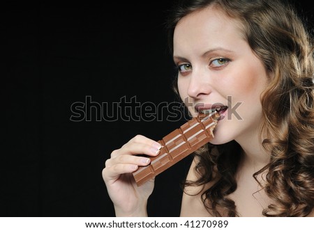 Young beautiful smiling woman eating milk chocolate isolated on black background