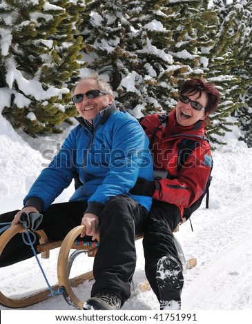 Lifestyle shot of active senior couple on sledge having fun in white winter country