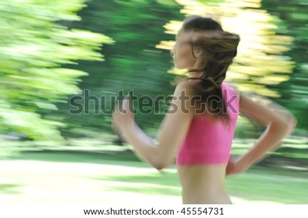 Young person (woman) running outside in park on sunny day - motion blurr