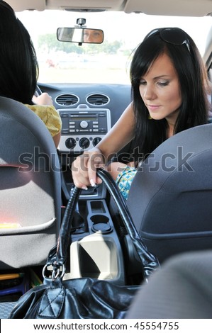 Friends traveling - young woman in car reaching handbag on back seat