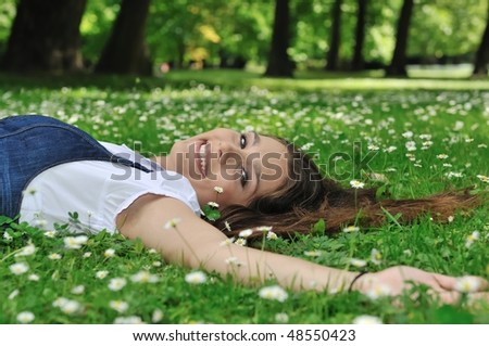 Detail of young woman lying in fresh green grass with flowers - above view