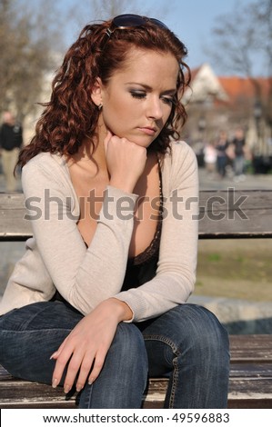 Young depressed woman (person) siting on bench in street outdoors