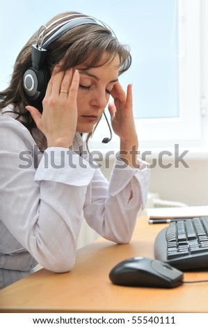 Young tired call center employee with headache sitting at computer on workplace