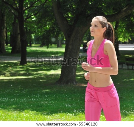 Young beautiful woman in pink running (jogging) outdoors in park on sunny day