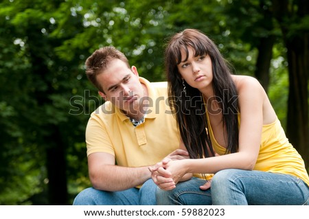 Young couple sitting outdoors on bench having relationship problems