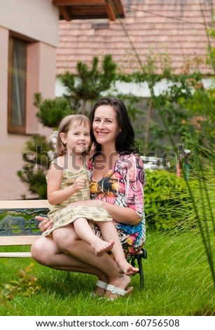 Portrait of Mother with daughter siting on bench in garden - family house in background