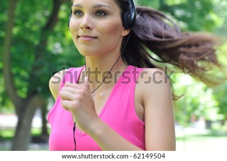 Young person (woman) with headphones listening music running outdoors in park on sunny day