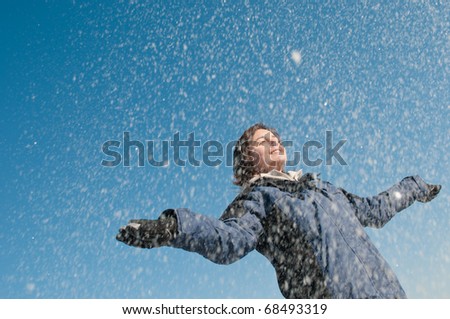 Young woman throwing snow on blue sky in background - joy and happines emotions