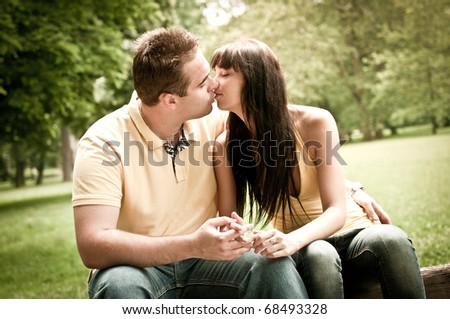 Young couple in love kissing outdoors - sitting on bench