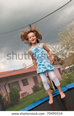 Small cute child jumping on trampoline - garden and family house in background
